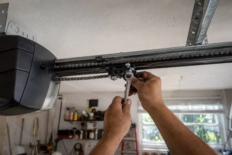 Hands holding a wrench against an opener trolley beneath a chain rail — Chain-Drive Opener Repair, Wilmot