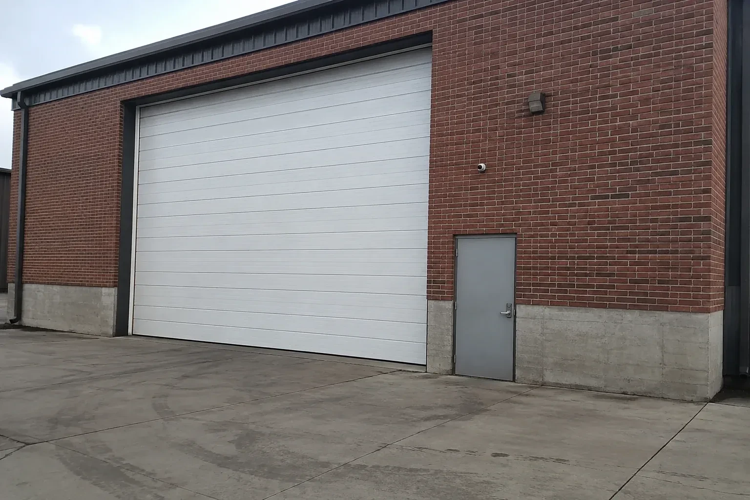 Tall closed sectional loading door beside a personnel door at a brick unit. — Commercial Sectional Door Repair, Wilmot