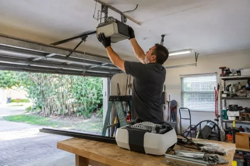 Person holding an overhead garage-door opener beside another opener and hardware on a workbench — Garage Door Opener Replacement, Wilmot