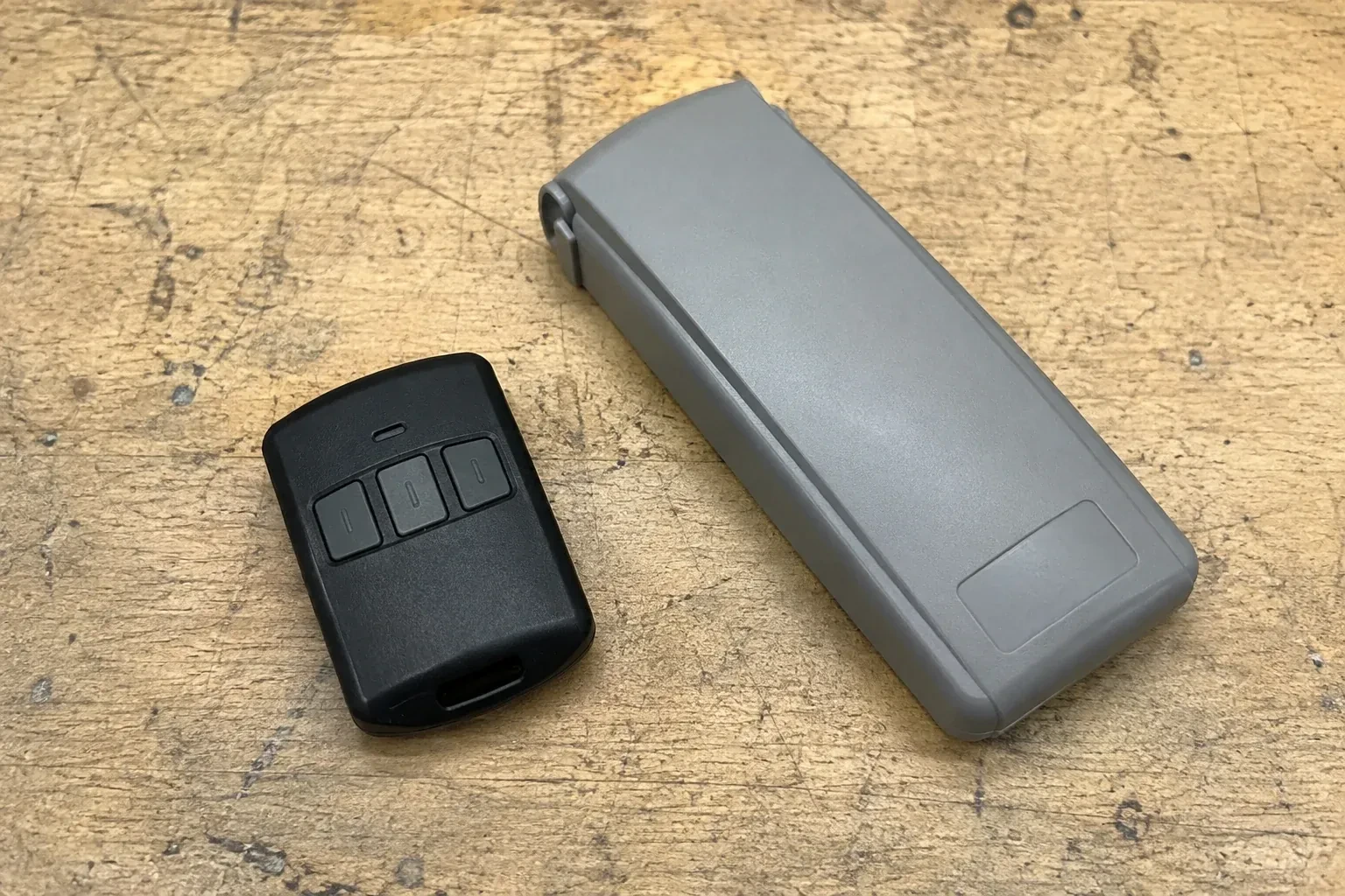 Three-button remote beside a closed grey keypad cover on a workbench. — Garage Door Remote and Keypad Programming, Wilmot