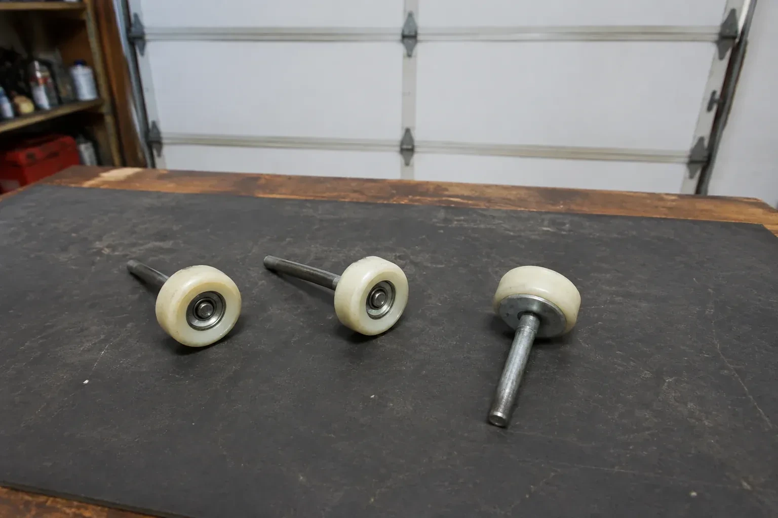 Three detached nylon-wheel garage door rollers with steel stems on a work mat. — Garage Door Roller Replacement, Wilmot